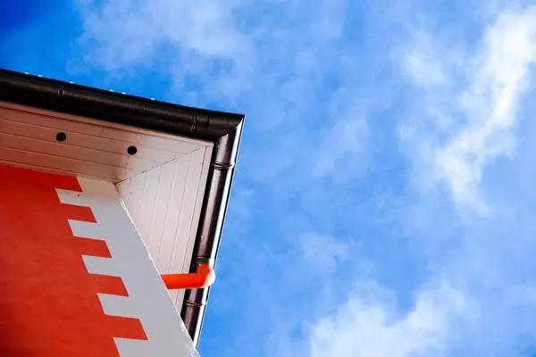 Dakgoot en oranje regenpijp onder een witte dakrand
