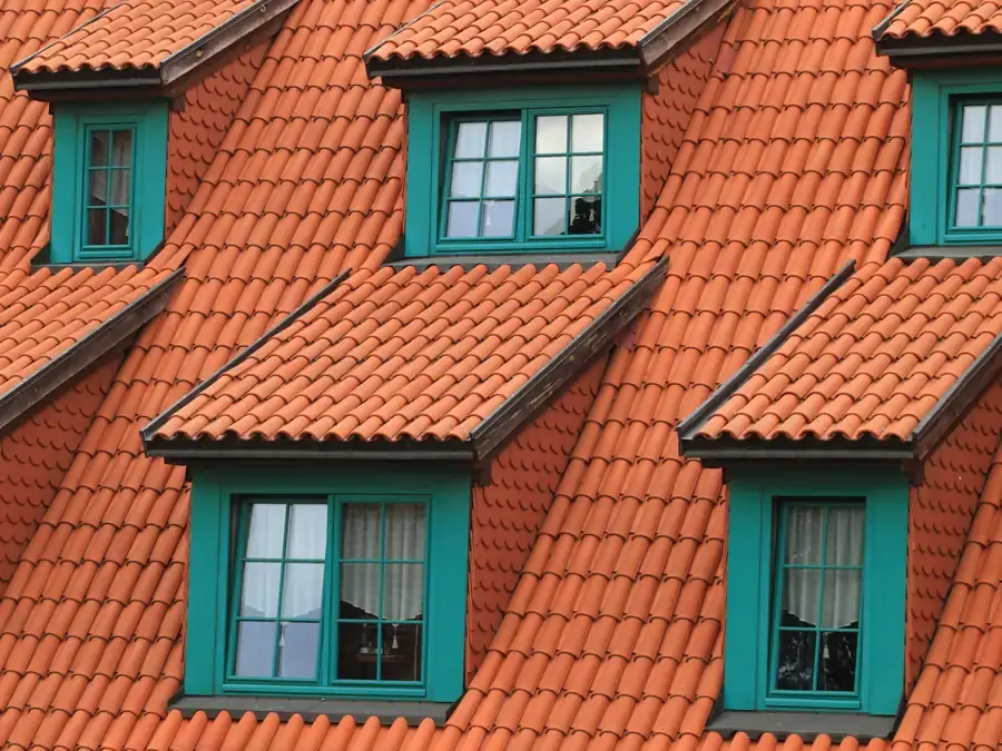 Oranje dakpannen rond groene dakkapellen op een hellend dak, voorbeeld van dakwerken in Rotterdam