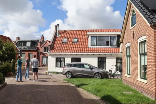 Oprit van klinkers naast een wit huis, met een geparkeerde auto