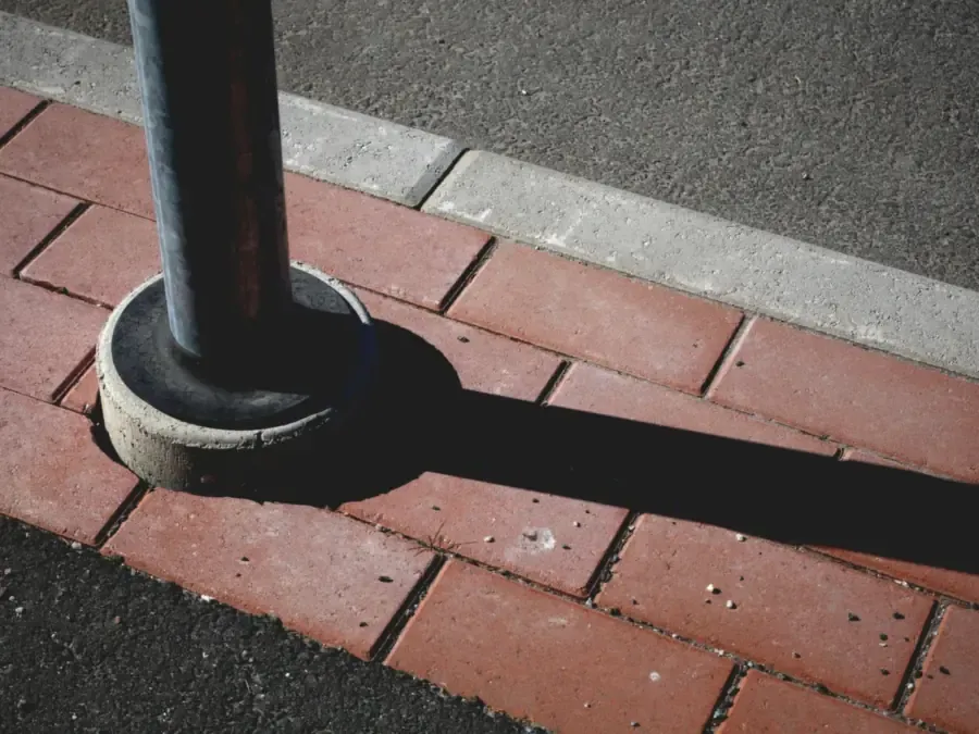 Rode betonklinkers met een grijze opsluitband langs het asfalt en een paaltje op een betonnen voet, detail van een oprit - opritten in Rotterdam