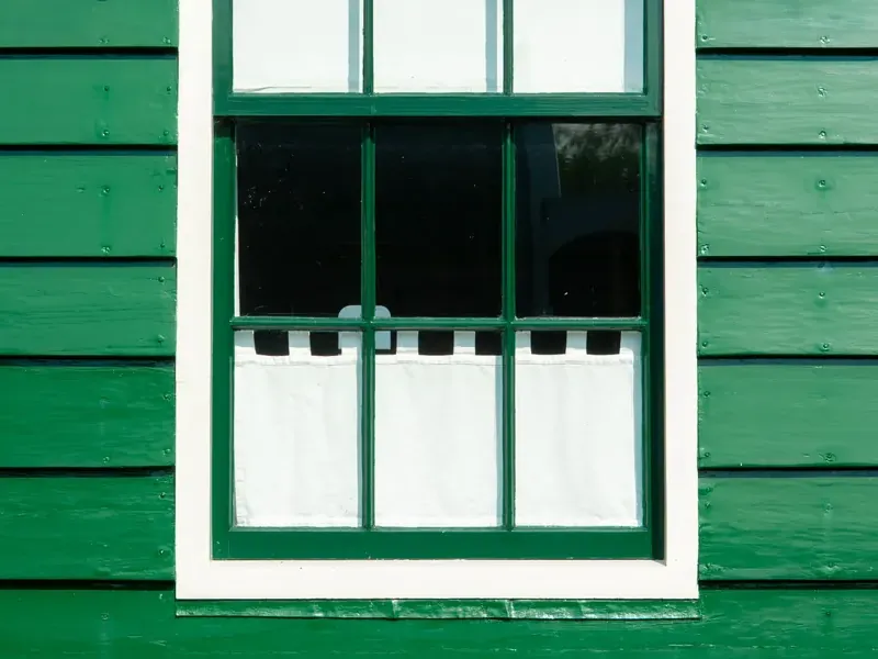 Groene houten gevel met een wit geschilderd raamkozijn - buitenschilderwerk aan kozijnen in Rotterdam